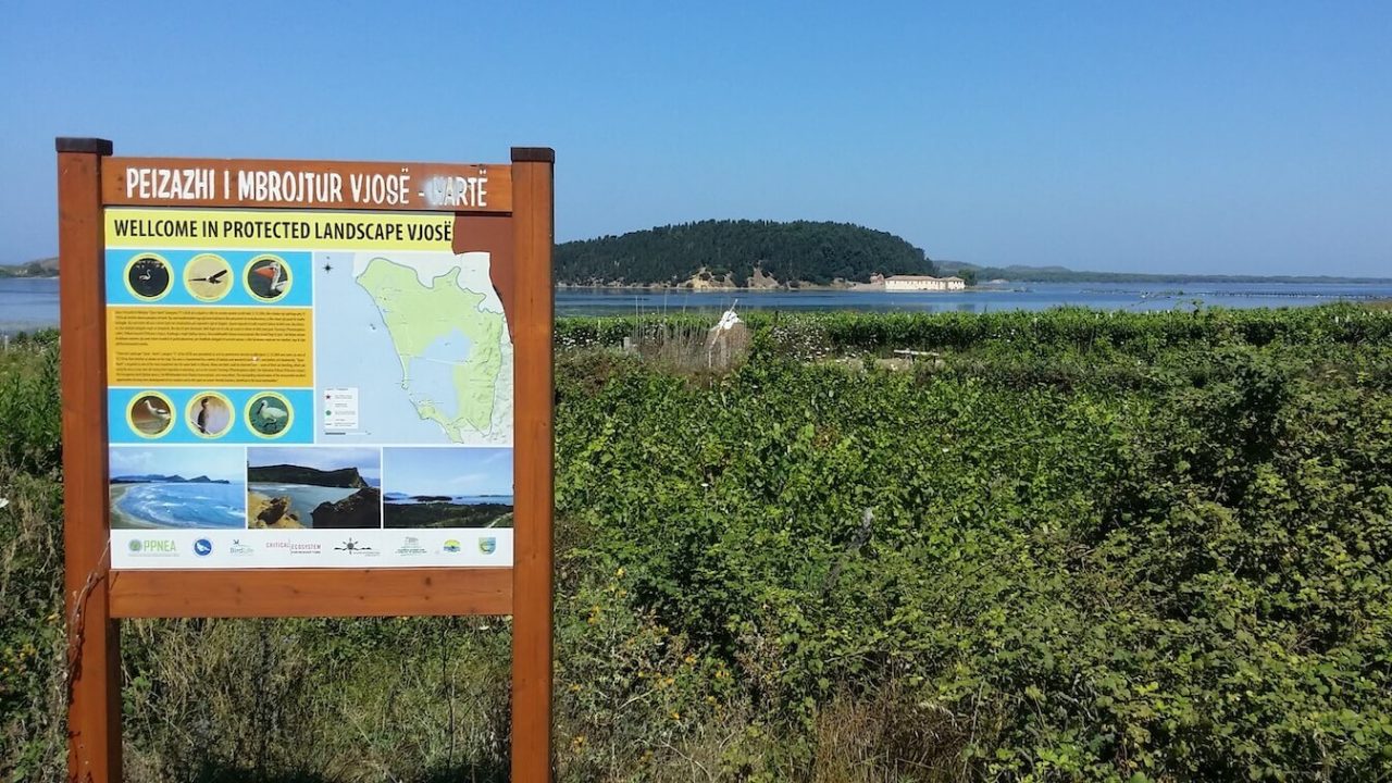 Protectee landscape sign in front of greenery and, beyond that, water.