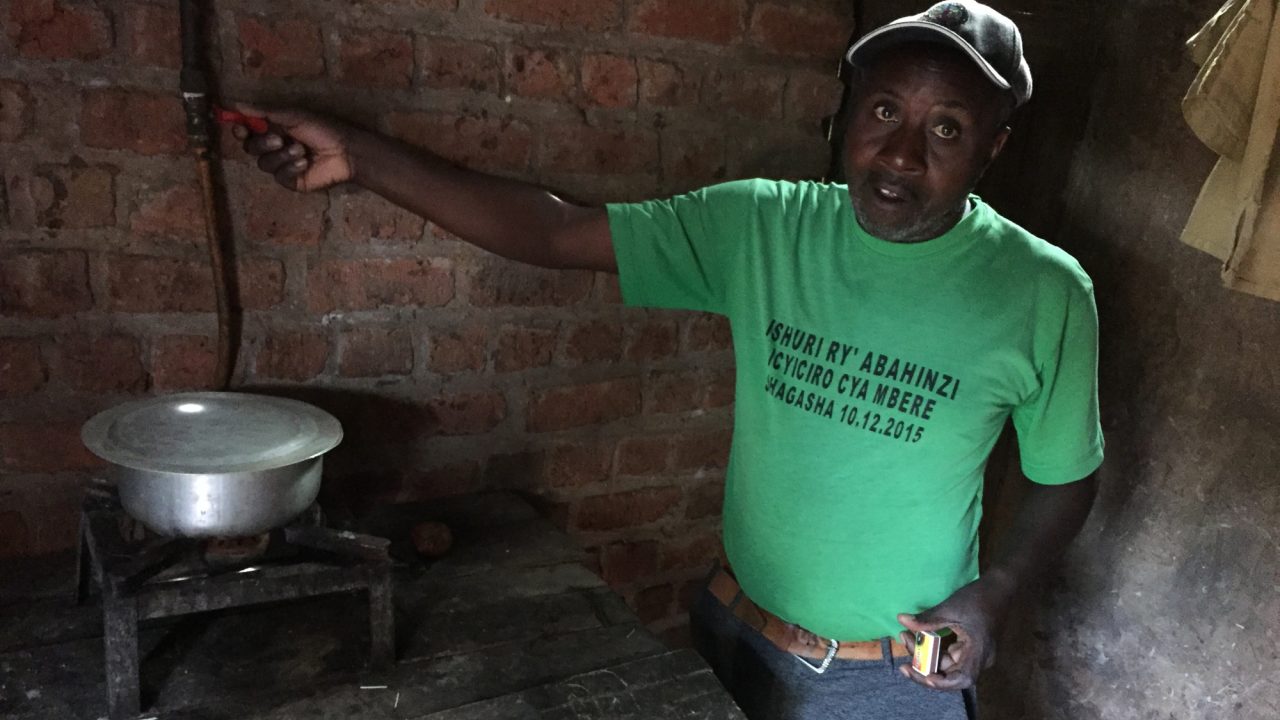 A man shows a biogas-powered stove set up on a table next to him