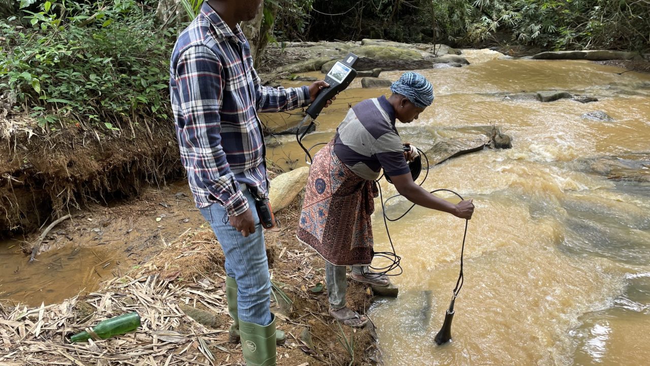 Frau Tetteh Aku, ein CREMA-Mitglied aus Obuoho, unterstützt die Bewertung der Wasserqualität des Ayensu-Flusses mithilfe eines Wasserqualitätsparameteranalysators der U50-Serie.