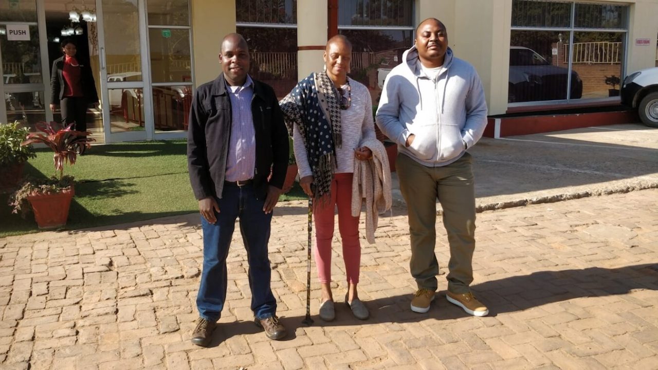 Two men and one woman standing outside building, smiling at camera.