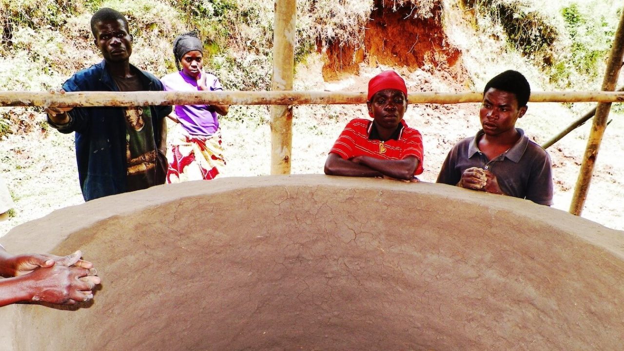 A few people standing over large kiln.
