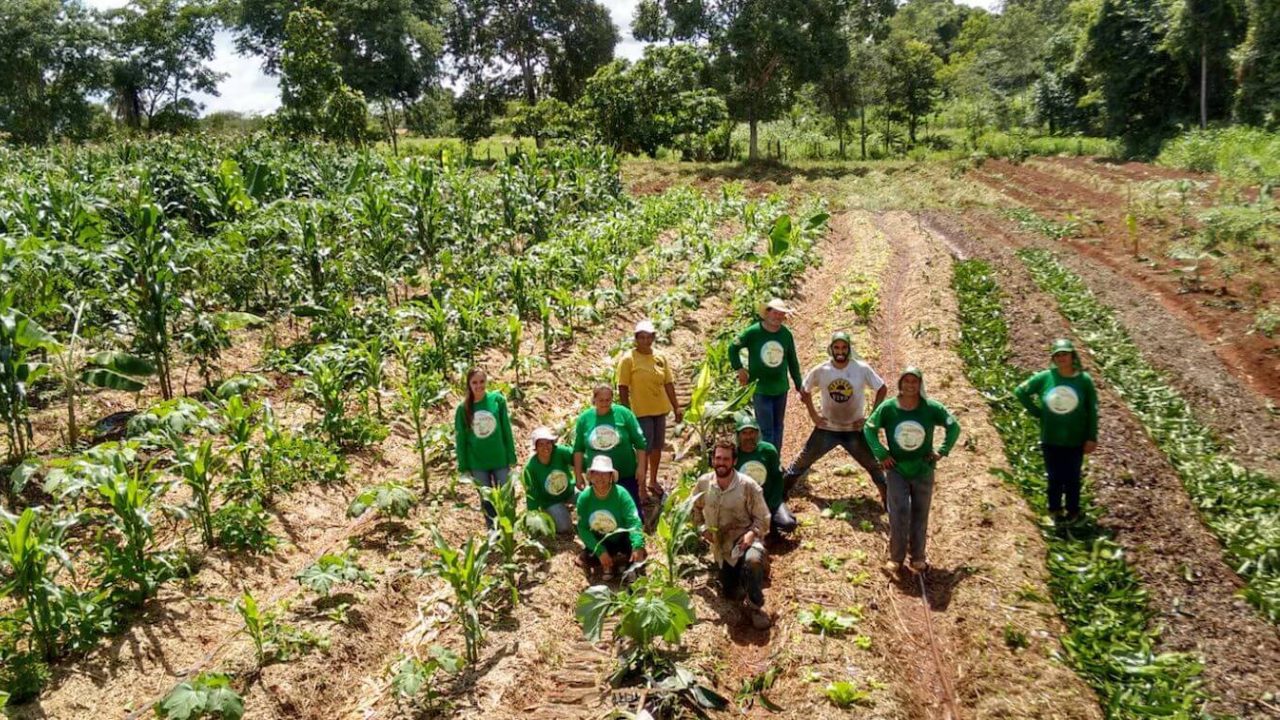 Unas 10 personas se paran en un campo agrícola, sonriendo a la cámara.
