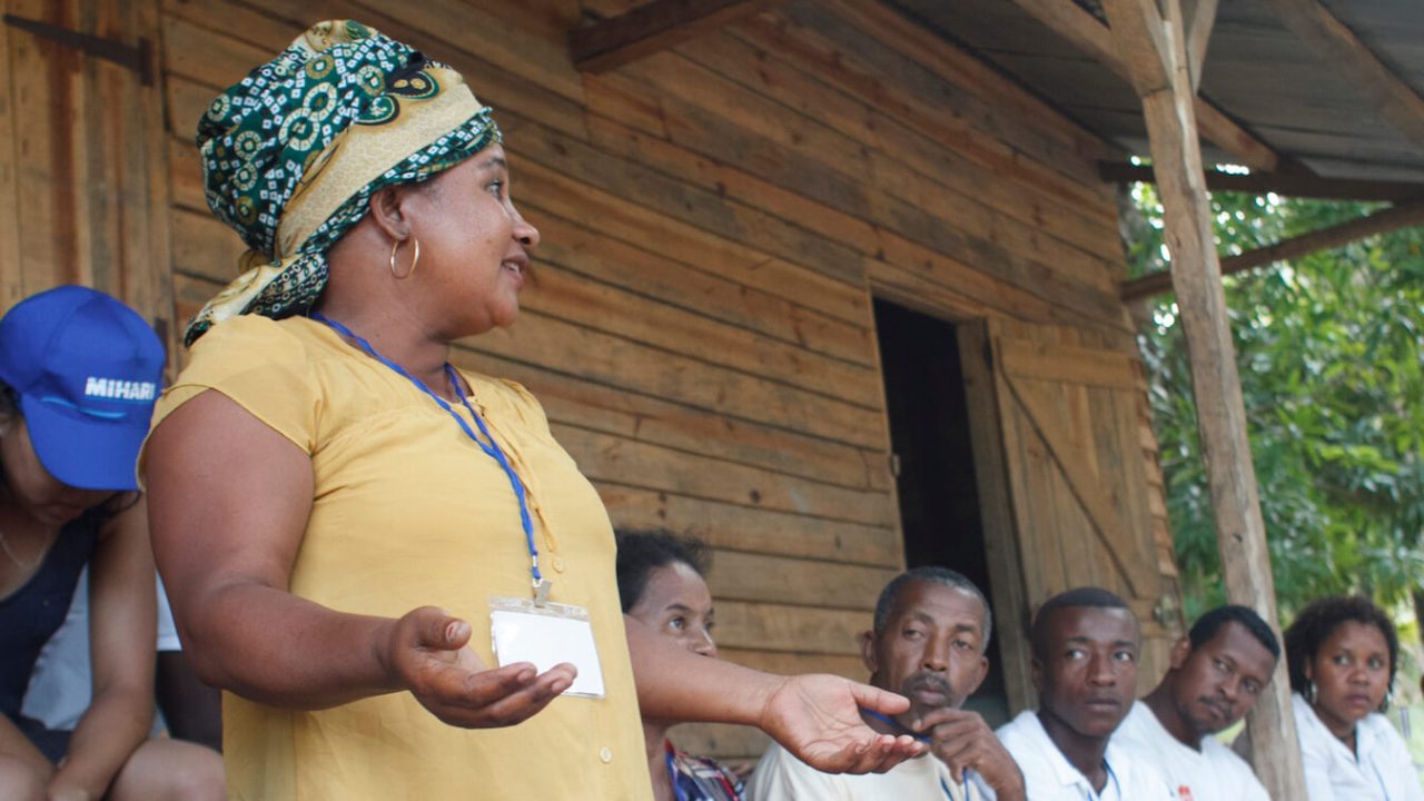 Woman stands, presenting to small group.