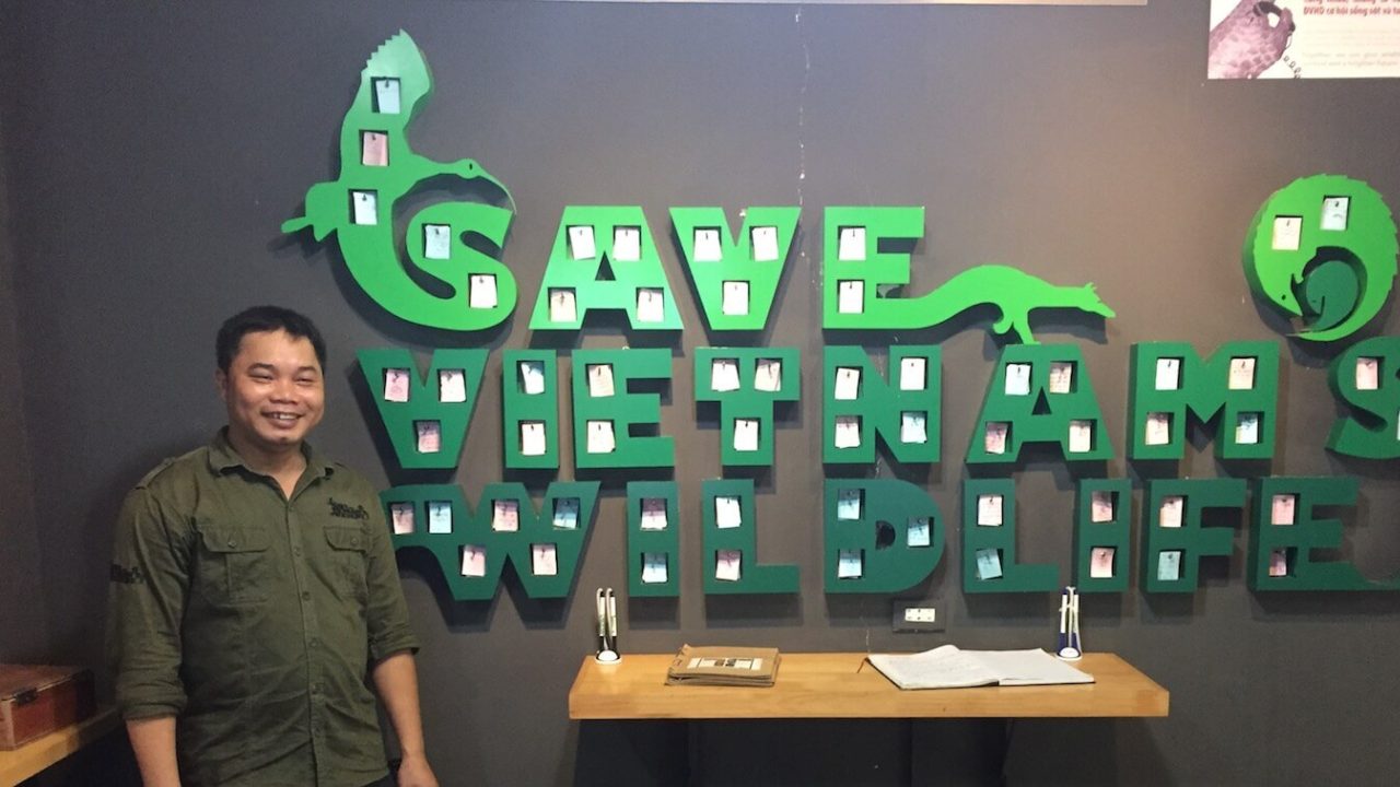 Man standing next to large, green indoor wall sign that reads "Save Vietnam's Wildlife."