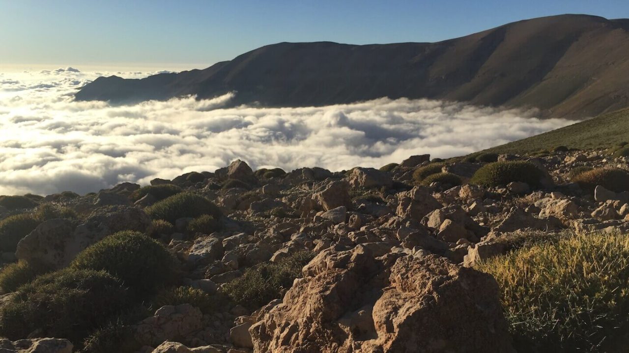 Landscape of clouds and mountains in the background, rocky ground in the foreground.