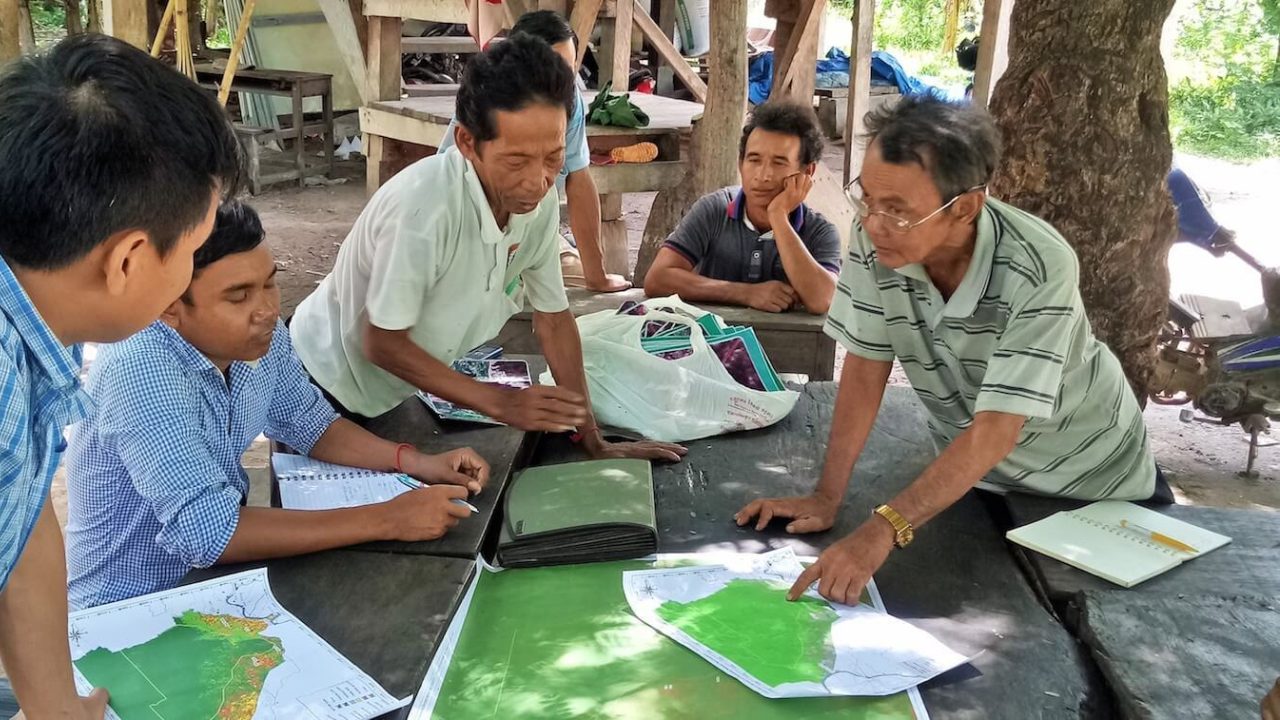 Une poignée d'hommes à l'extérieur regardent des cartes vertes sur une table.