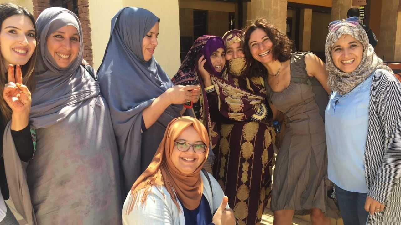 Group of about 8 women, most wearing head scarves, smile at camera.