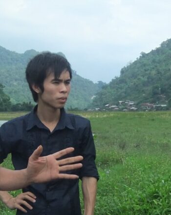 Two men and one woman having a discussion in the foreground, lush landscape in the background.