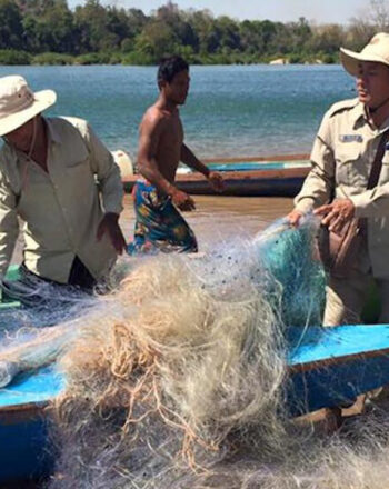 Five men on the beach, pulling large amounts of tangled nets from a docked fishing boat.