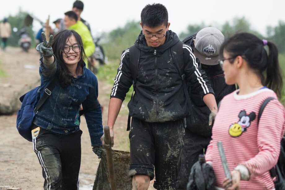 Teenagers smiling, one holding peace sign, carrying trash bags