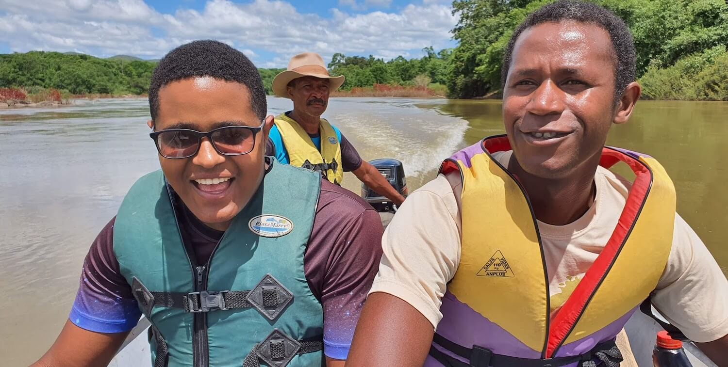 Three men in small motorboat wearing lifejackets and smiling.