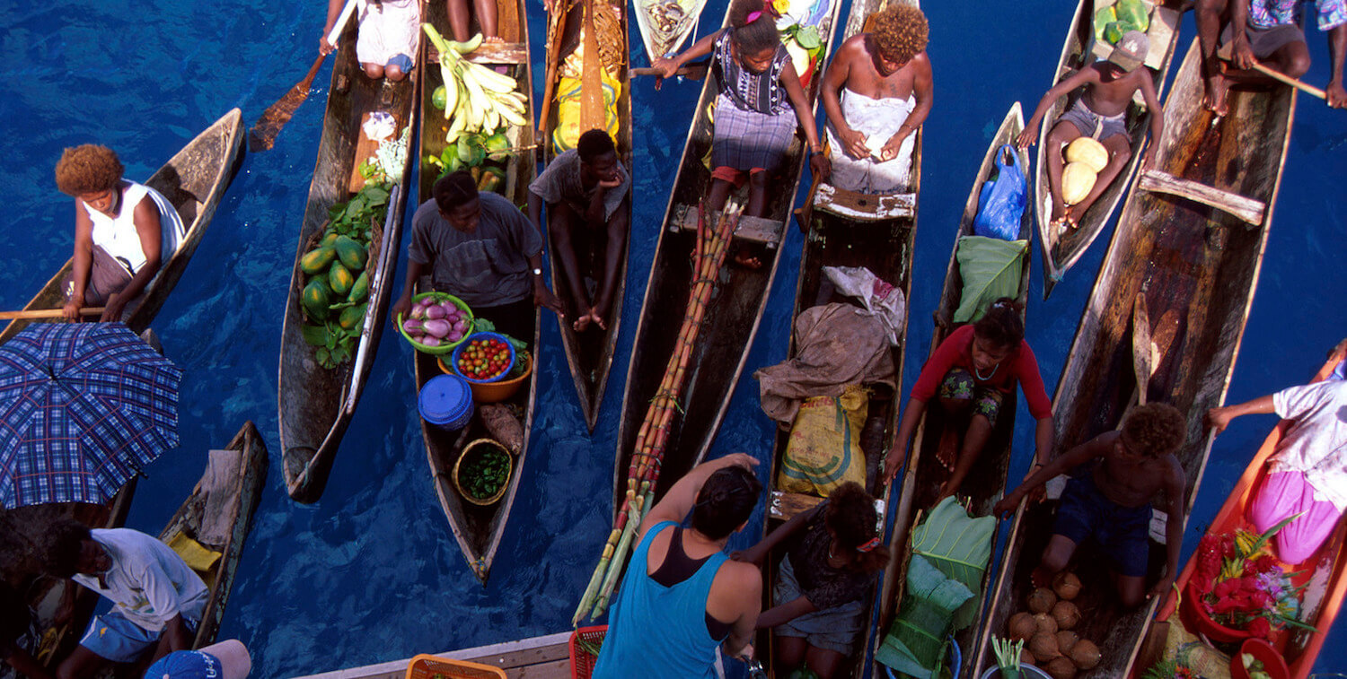 Aeriel view of crowded canoes on water, carrying produce.