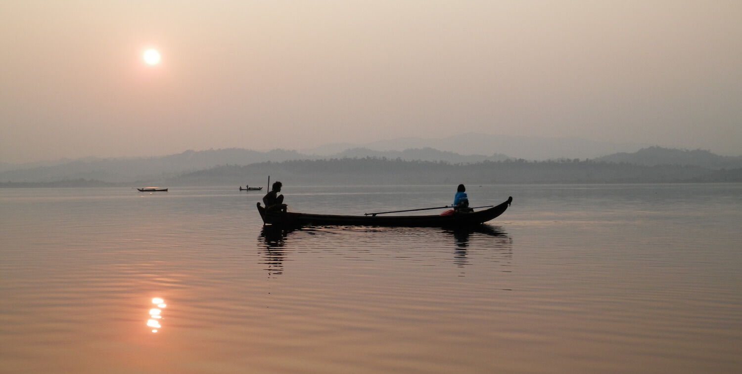 Silhouette of person in canoe on lake, sunset or sunrise.