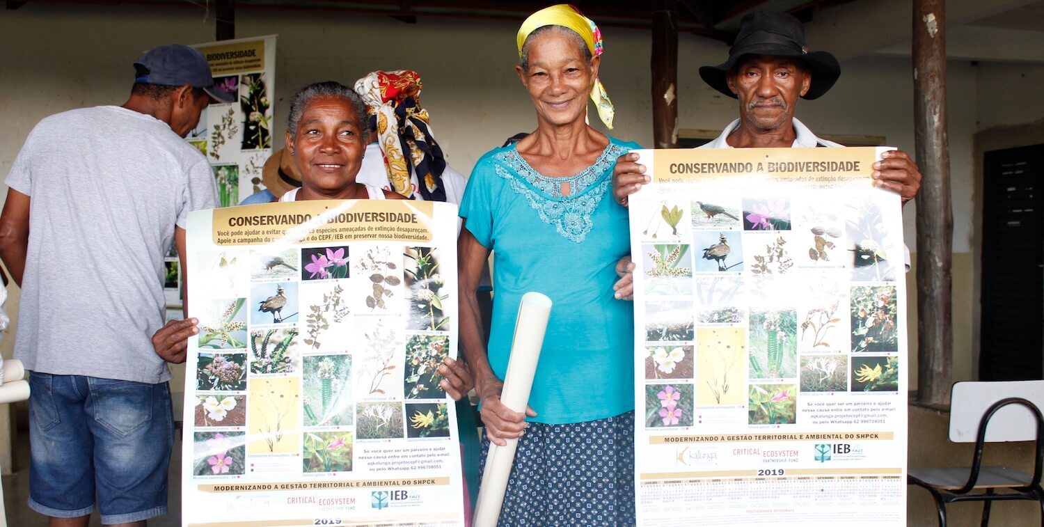 Three people, two women and one man, face camera. Two hold posters.