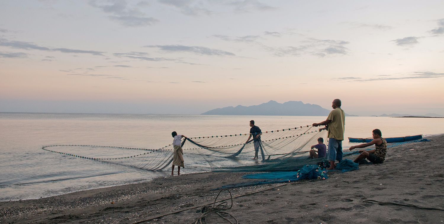 Small group of men stand on a beach, pulling a large net from the water, Flores Island, Indonesia.